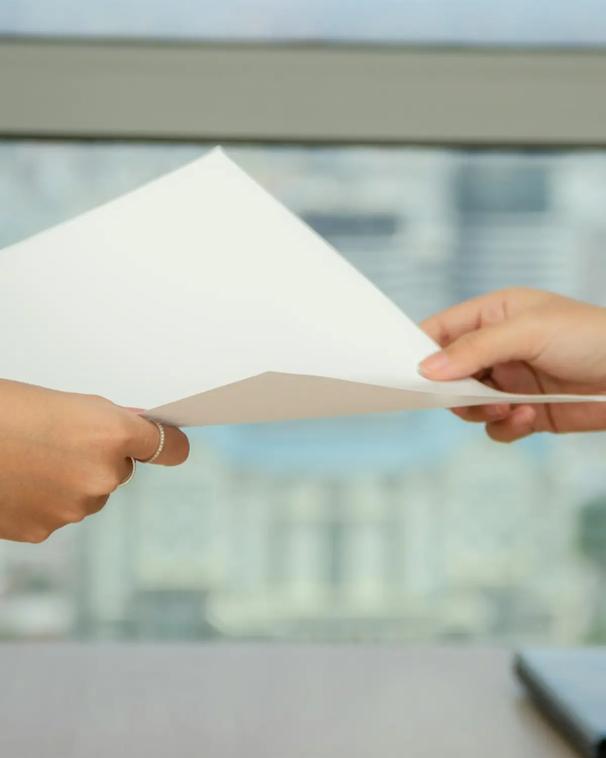 Two hands passing a sheet of paper in front of a city window