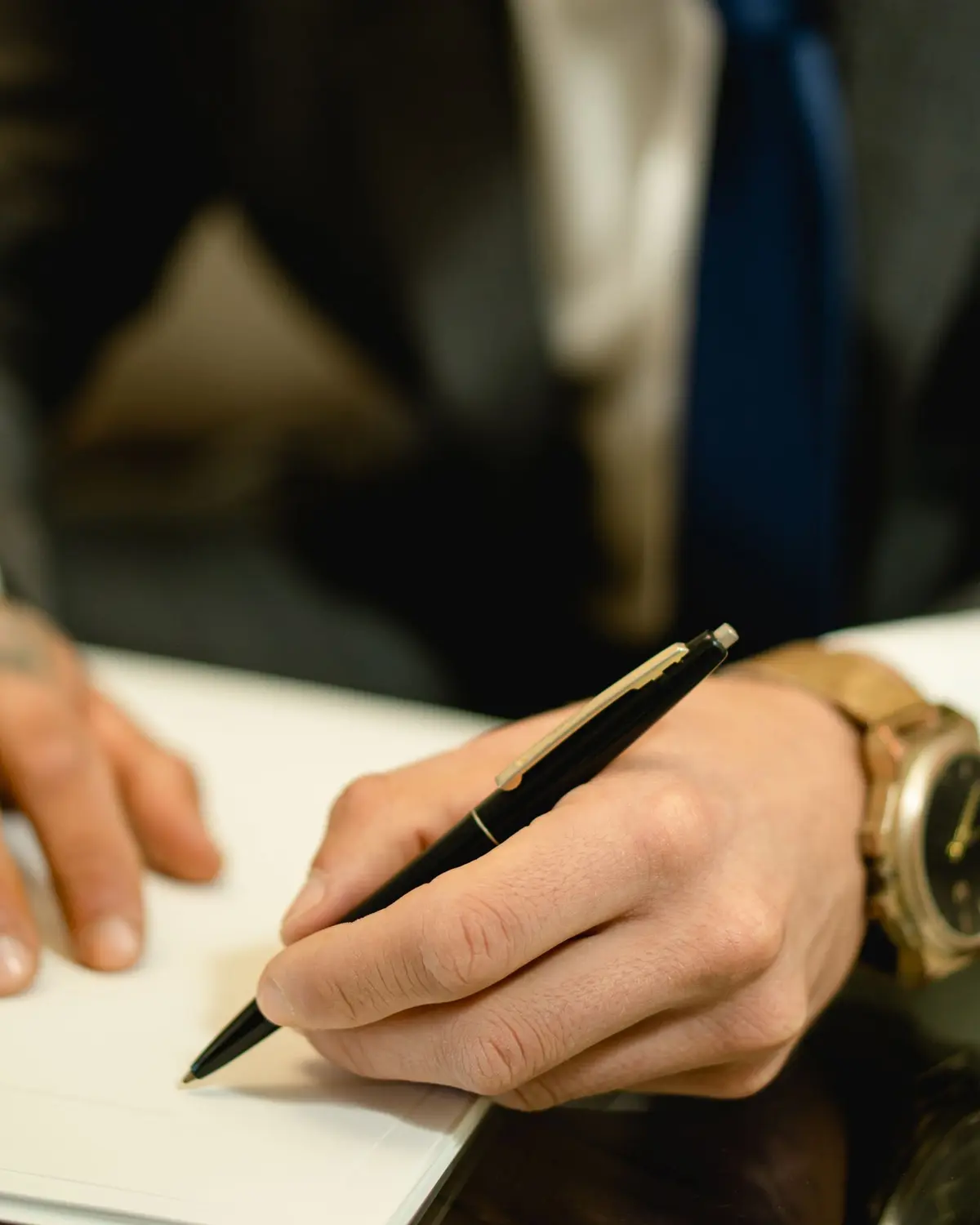 A hand in a suit signing a document